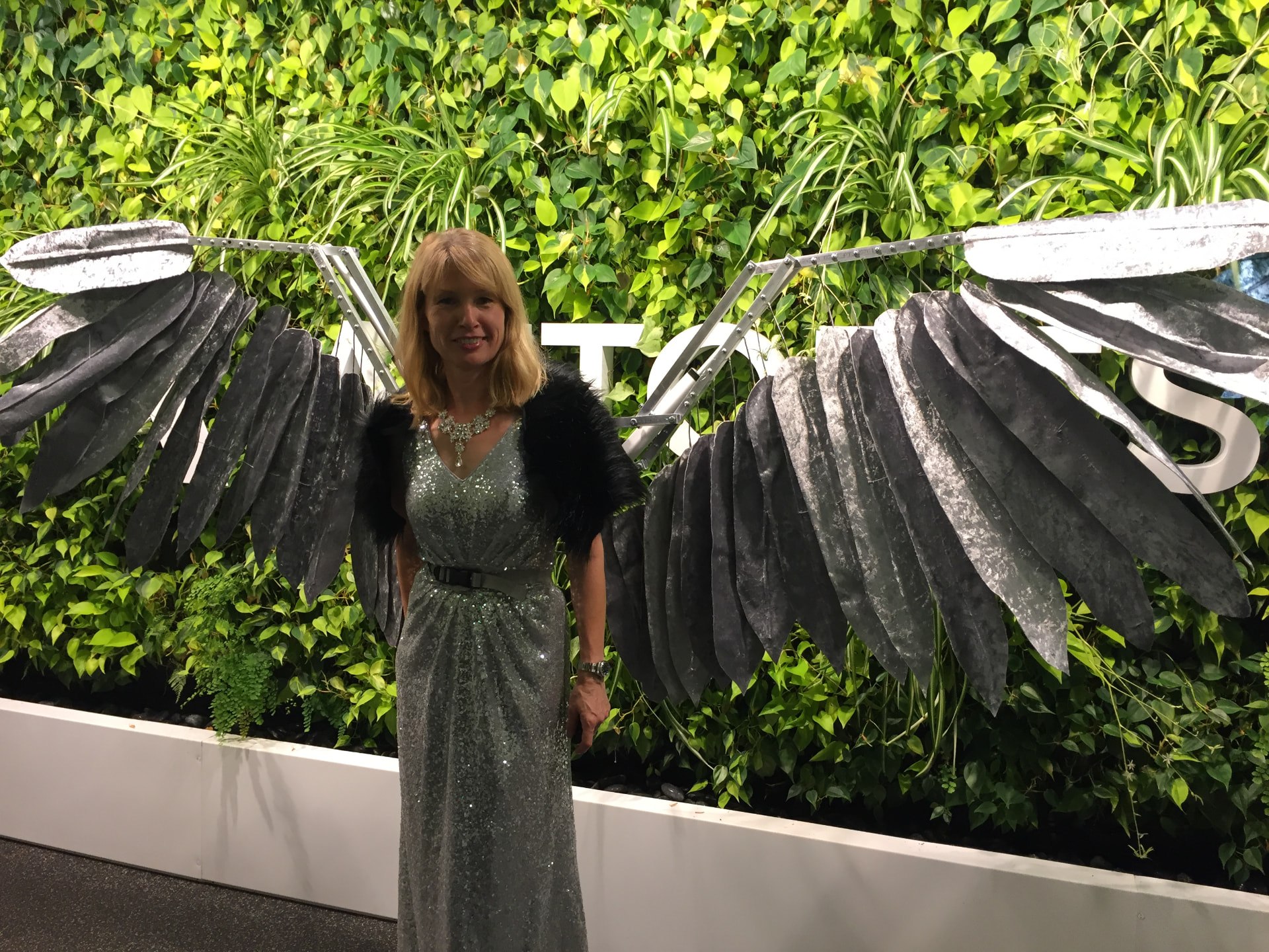 A maker in black mechanical wings in front of a living plant wall